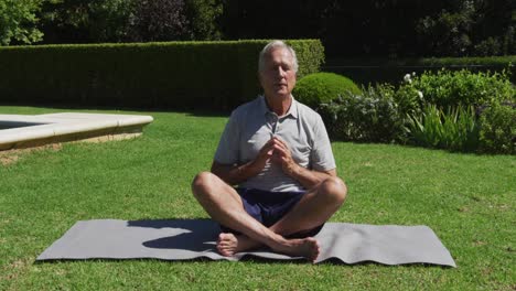 caucasian senior man practicing yoga meditating in garden in the sun