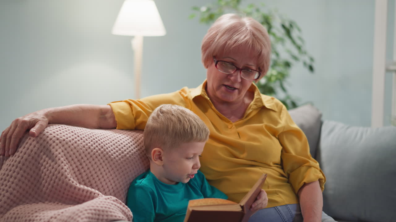 Il piccolo nipote cerca di leggere un libro alla nonna amorevole a casa.