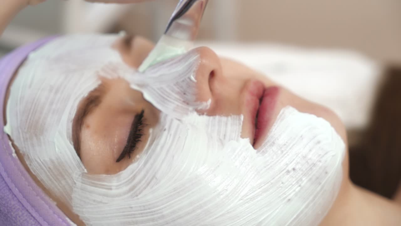 Donna con maschera viso. Estetista che applica una maschera viso all'argilla sul viso di una donna.