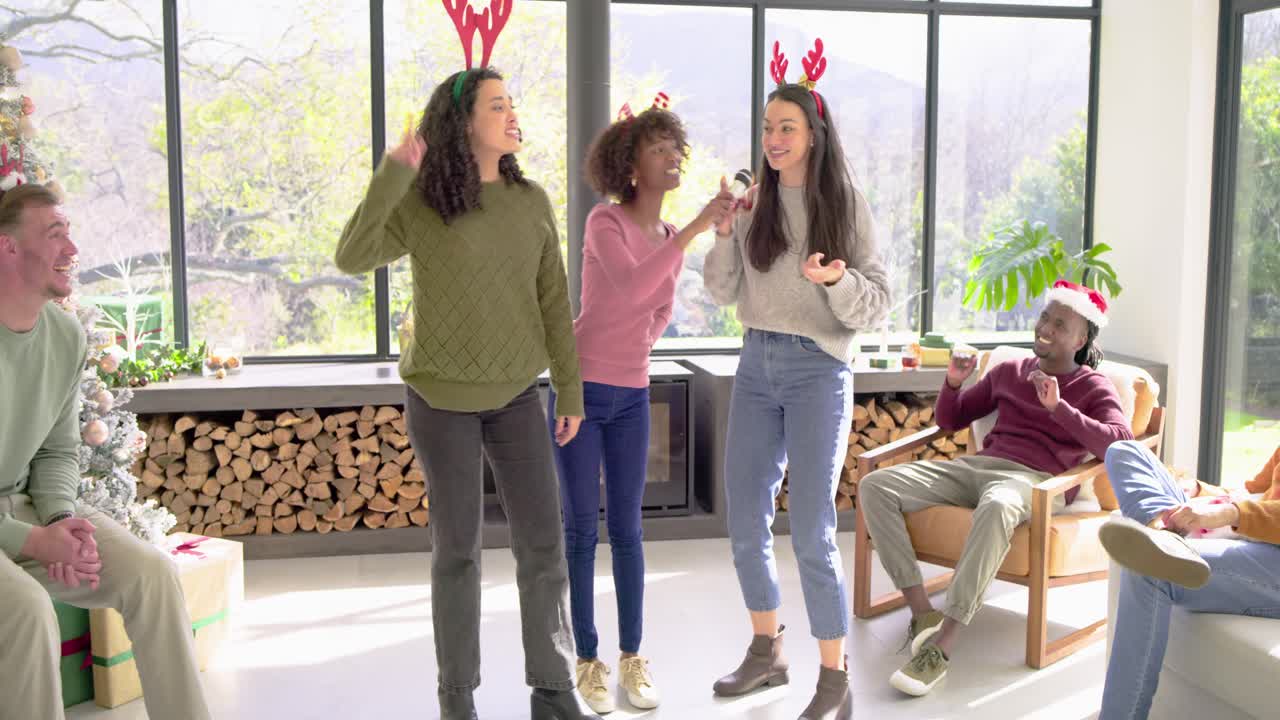 Entering living room wearing antlers three women singing into mic and dancing at holiday party