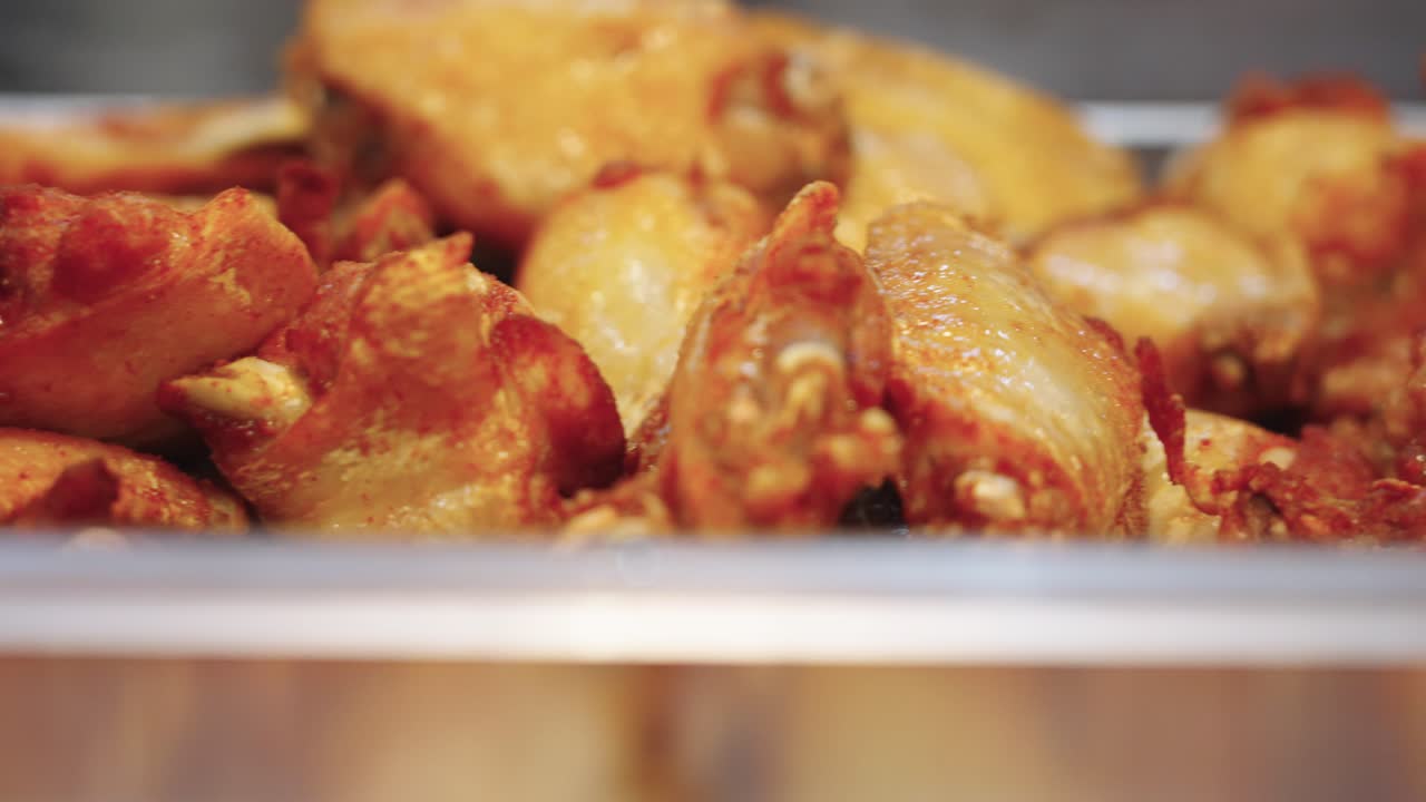 Riprese 4K super ravvicinate con panoramica a destra di ali di pollo appena fritte in un grande contenitore, che mostrano una consistenza dorata e croccante e cibo caldo e saporito da una cucina professionale.