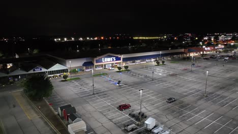 aerial approaching shot of lowe´s building at night with illuminated and monitored parking area. american city suburb in virginia, usa. descending wide shot.