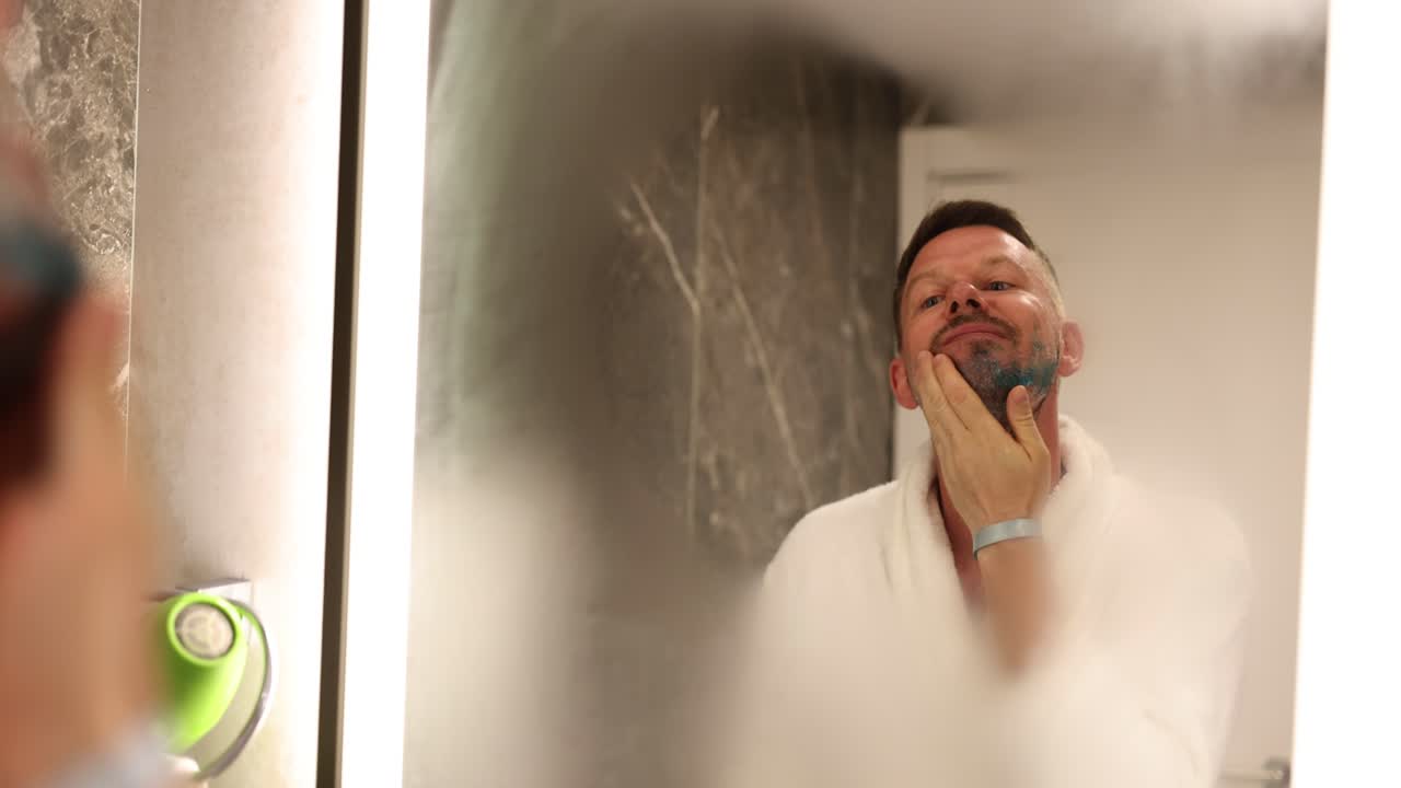 Uomo si applica il gel da barba sul viso guardandosi in uno specchio appannato