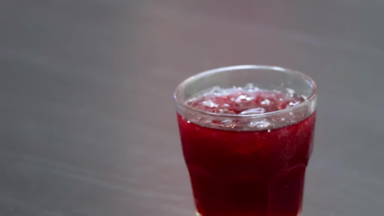 Close-up of hands placing glasses of chilled red drinks on a dark table surface.