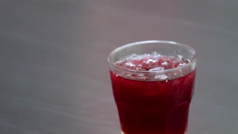 close-up of hands placing glasses of chilled red drinks on a dark table surface.