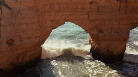 aerial tracking shot of sun kissed waves crashing against massive limestone cliffs in the algarve region of portugal