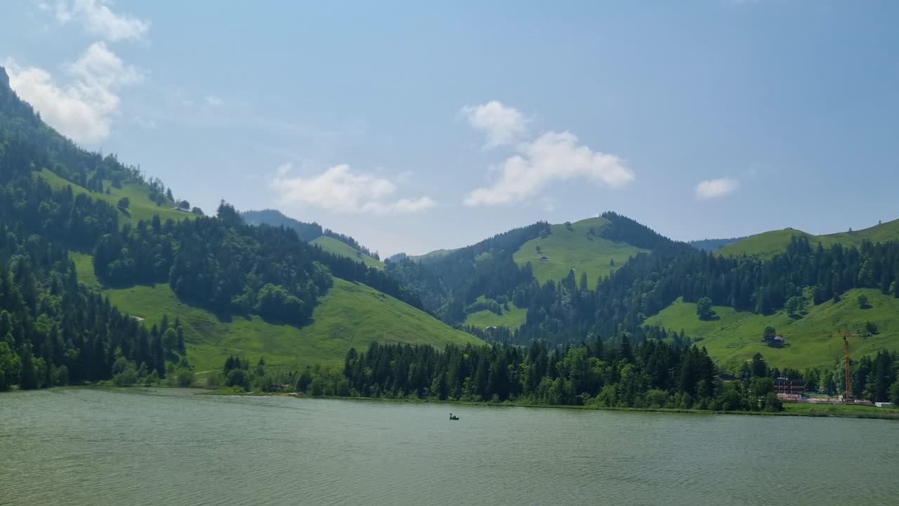 Panoramic view over Schwarzsee in Fribourg’s Alps, with lush green hills and mountains unfolding behind the dark lake, a beloved getaway for locals and visitors in Switzerland