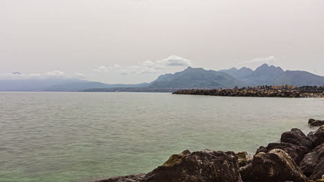 Timelapse-shot-of-rocky-seashore-with-mountain-range-in-the-background-in-Belvedere,-Italy-on-a-cloudy-day