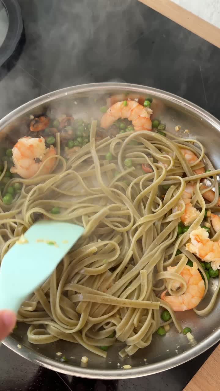 Preparazione di pasta con gamberi, frutti di mare e piselli in padella