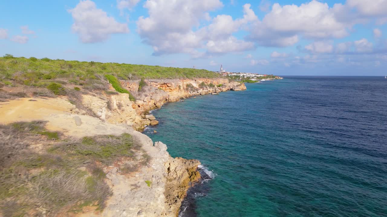 Drone footage of Jan Thiel, Curacao, highlighting the rugged coastline, vibrant blue waters, and natural cliffs