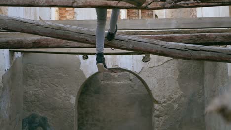 young man, teenager, swings his feet sitting several meters high on a collapsed beam in an abandoned house