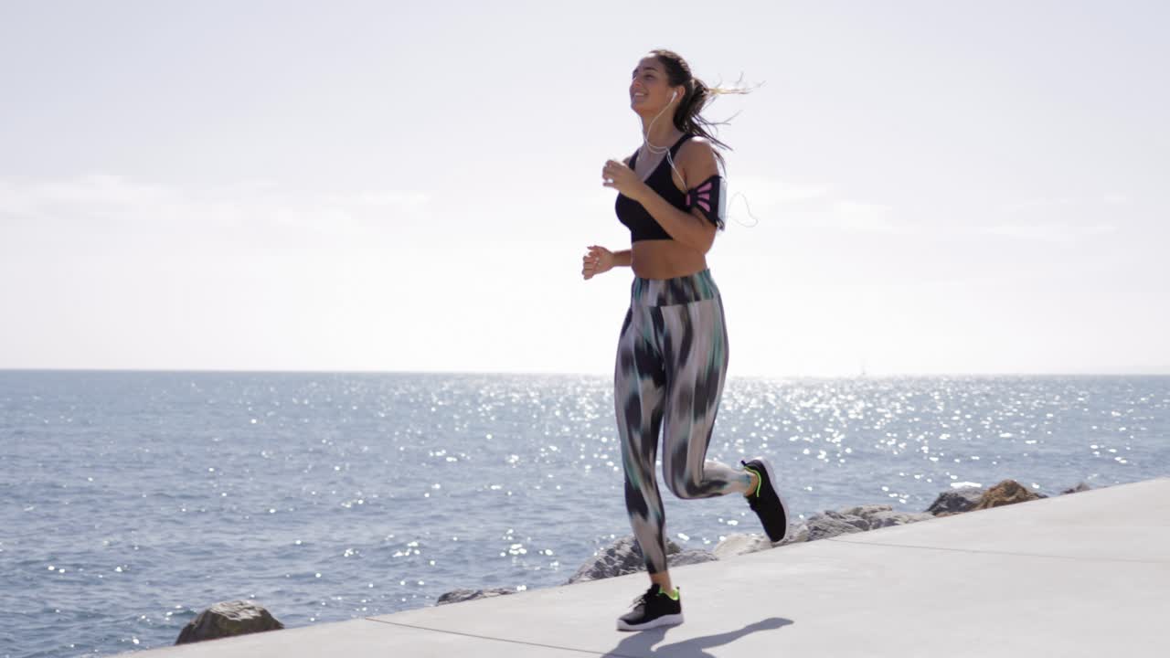 vista de una chica en forma con ropa deportiva corriendo a lo largo del paseo marítimo