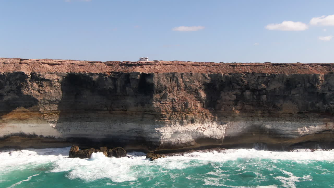 Campervan parked on top of steep cliffs over disturbed waters