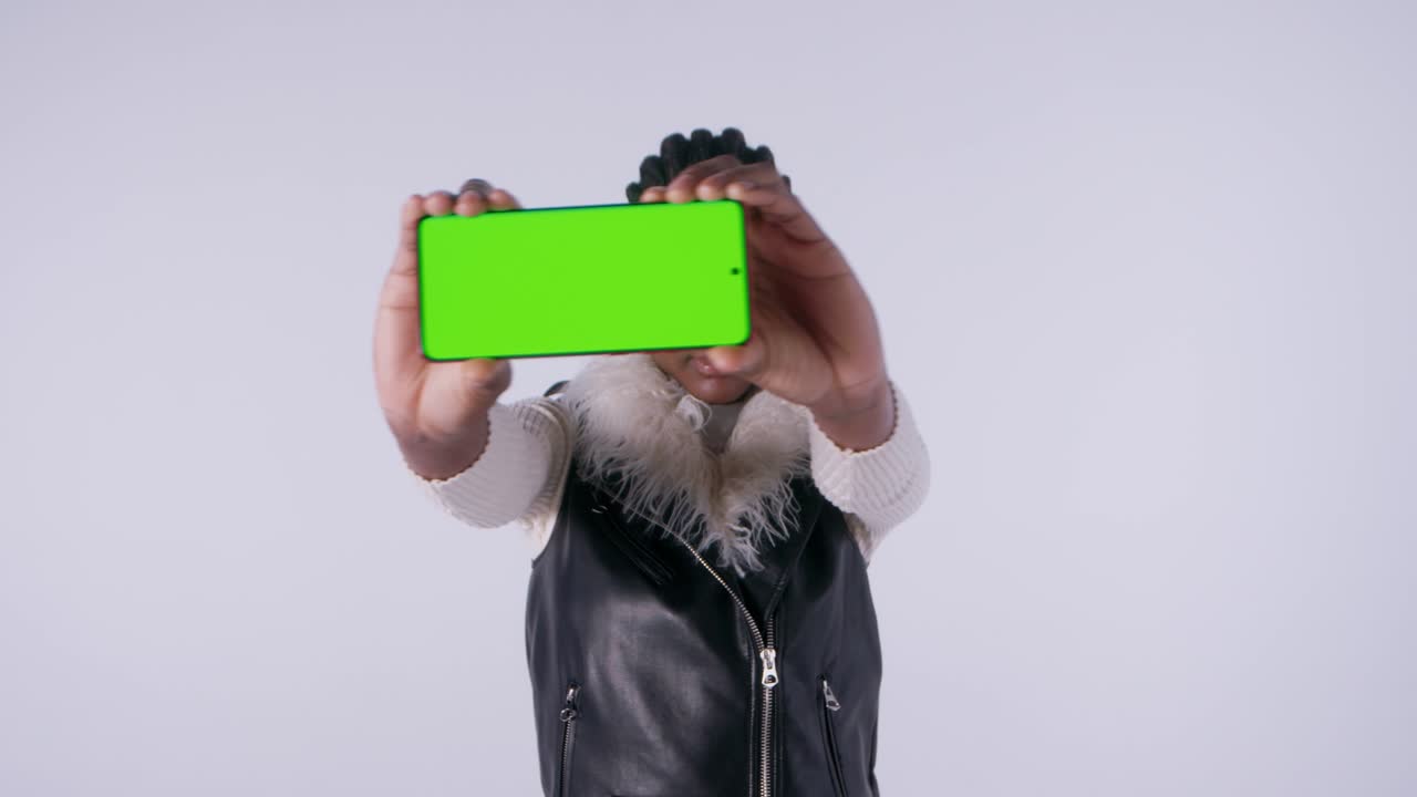 Woman holding smartphone with green screen towards camera in studio environment.