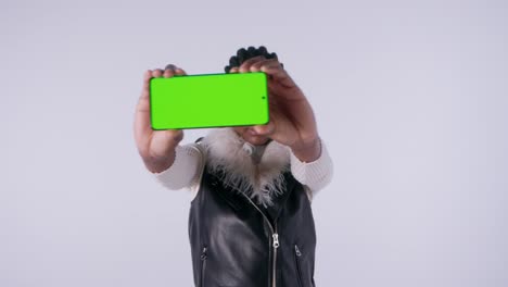 woman holding smartphone with green screen towards camera in studio environment.
