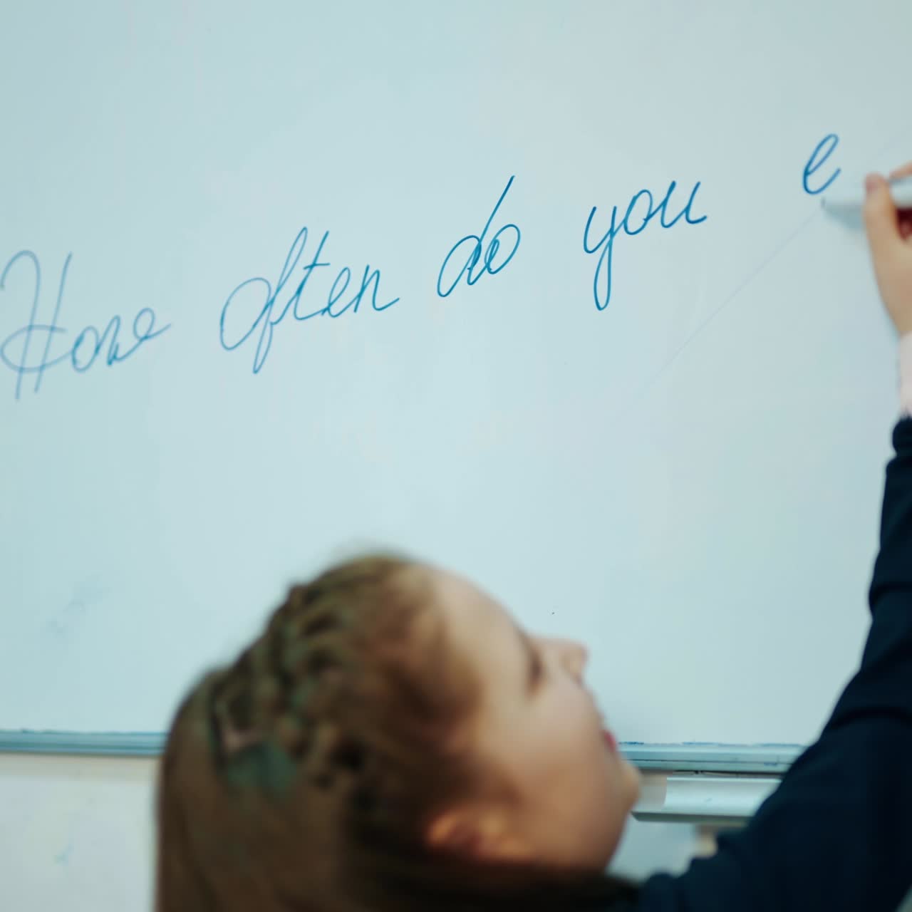 Learning process at school. Little girl writing with a marker on magnetic blackboard. Schoolgirl in the classroom. Elementary education.