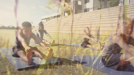 animation of grasses over happy diverse schoolboys stretching in outdoor yoga class