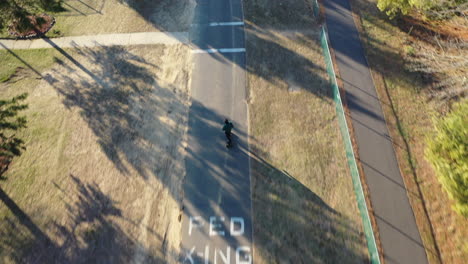 an aerial tracking of a man on an electric skateboard in an empty park on a sunny day