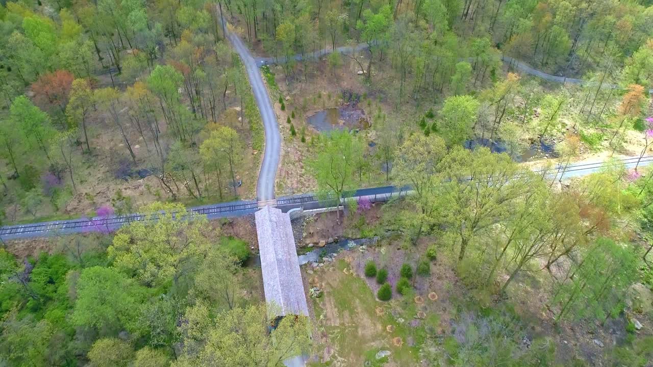 Aerial View of Spring Time Colors of a Forest with a Covered Bridge and Rail Road Track on a Sunny Day