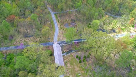 aerial view of spring time colors of a forest with a covered bridge and rail road track on a sunny day