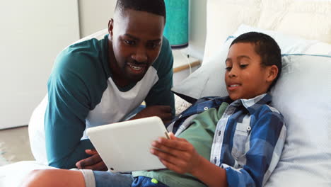 Son-showing-digital-tablet-to-his-father-in-bedroom