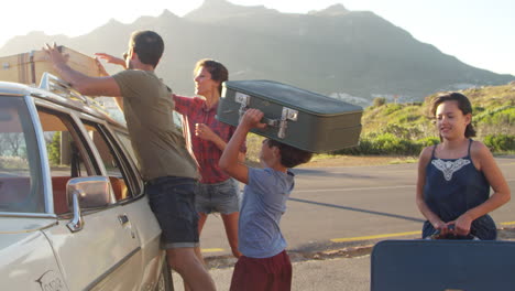 family loading luggage onto car roof rack ready for road trip