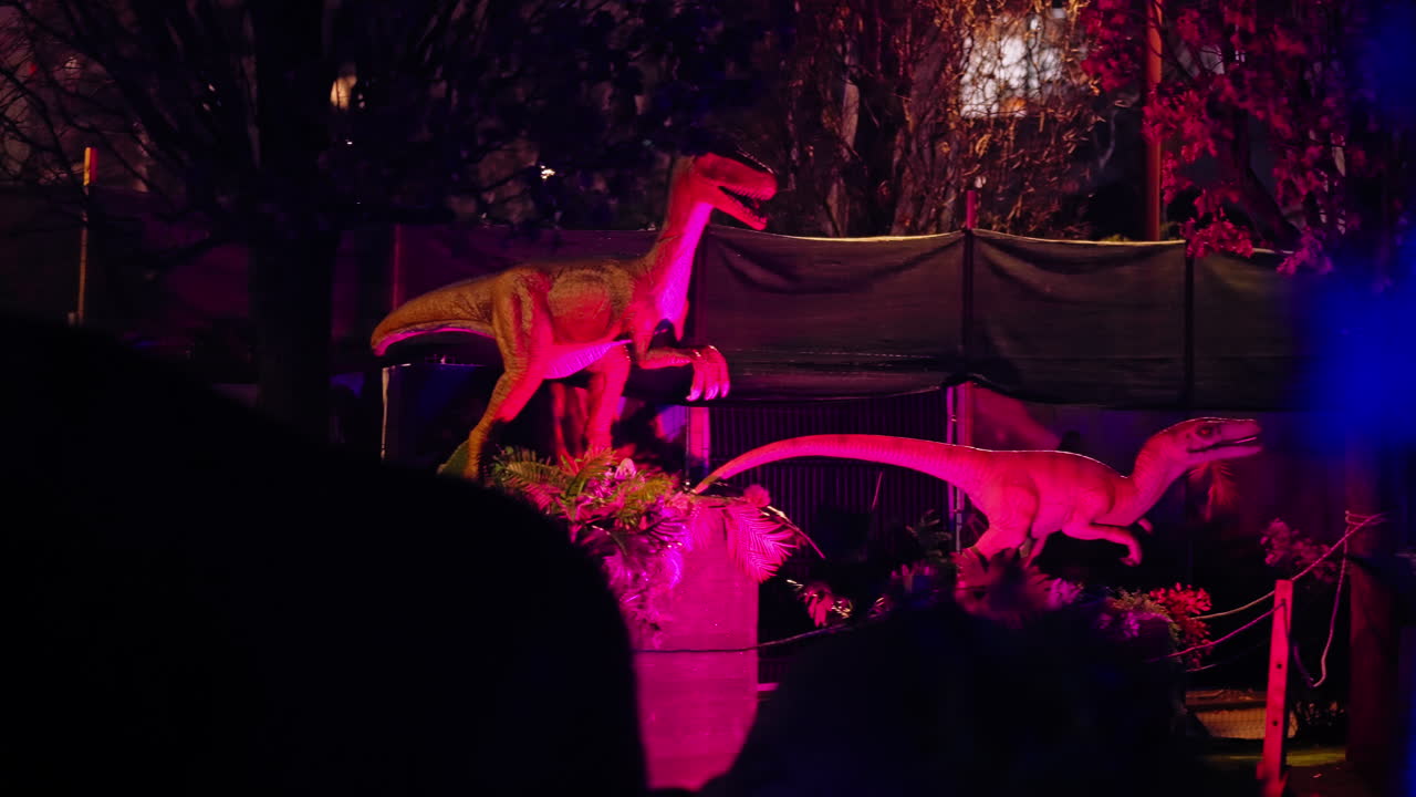 robot de dos dinosaurios rapaces moviéndose en un parque temático por la noche