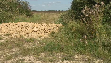 a pile of sand stones blocking a gateway to a field used to prevent vehicles from entering the field