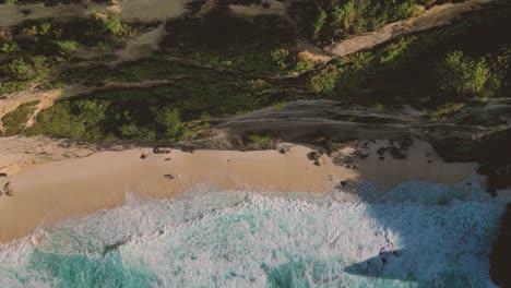 top view of a big cliff with waves crashing the sand of diamond beach, nusa penida - indonesia