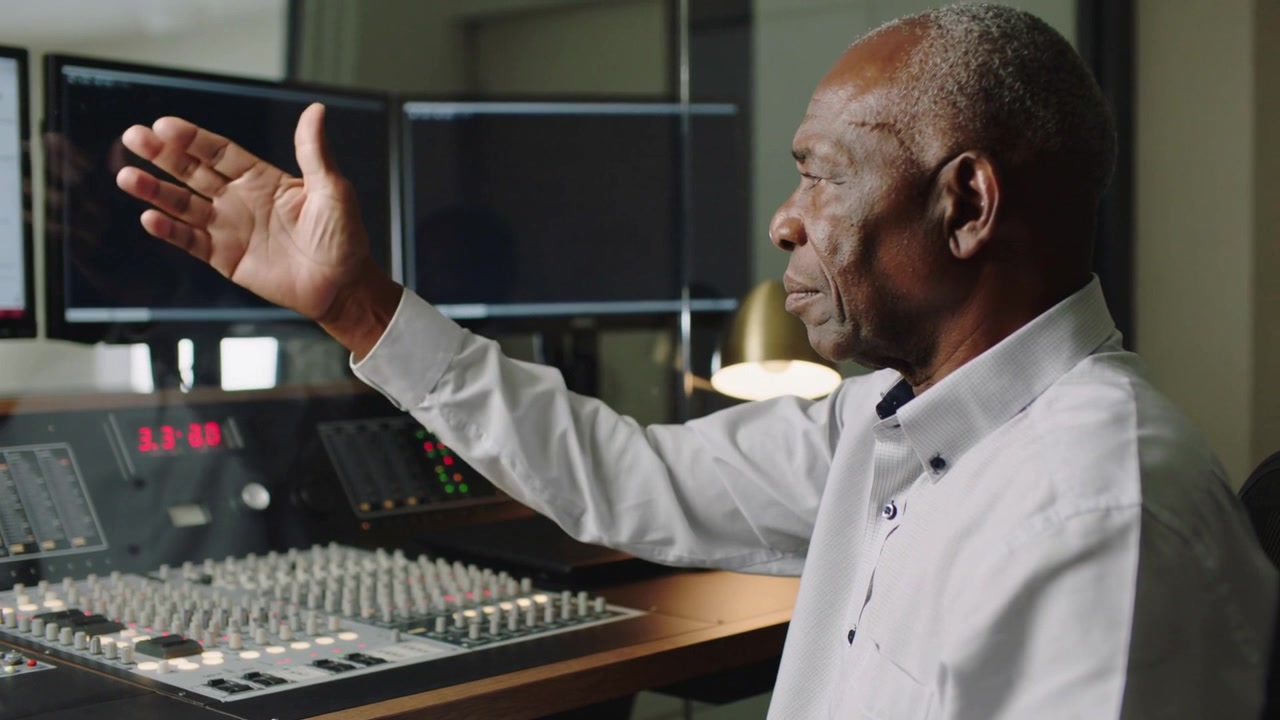 Starting demo engineer wearing white shirt showing console controls in studio, copy space