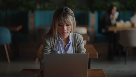 zoom camera asian young woman works and looks at the laptop screen sitting in a cafe
