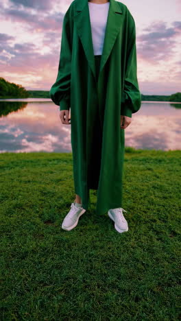 person in green dress and sneakers by a lake at sunset