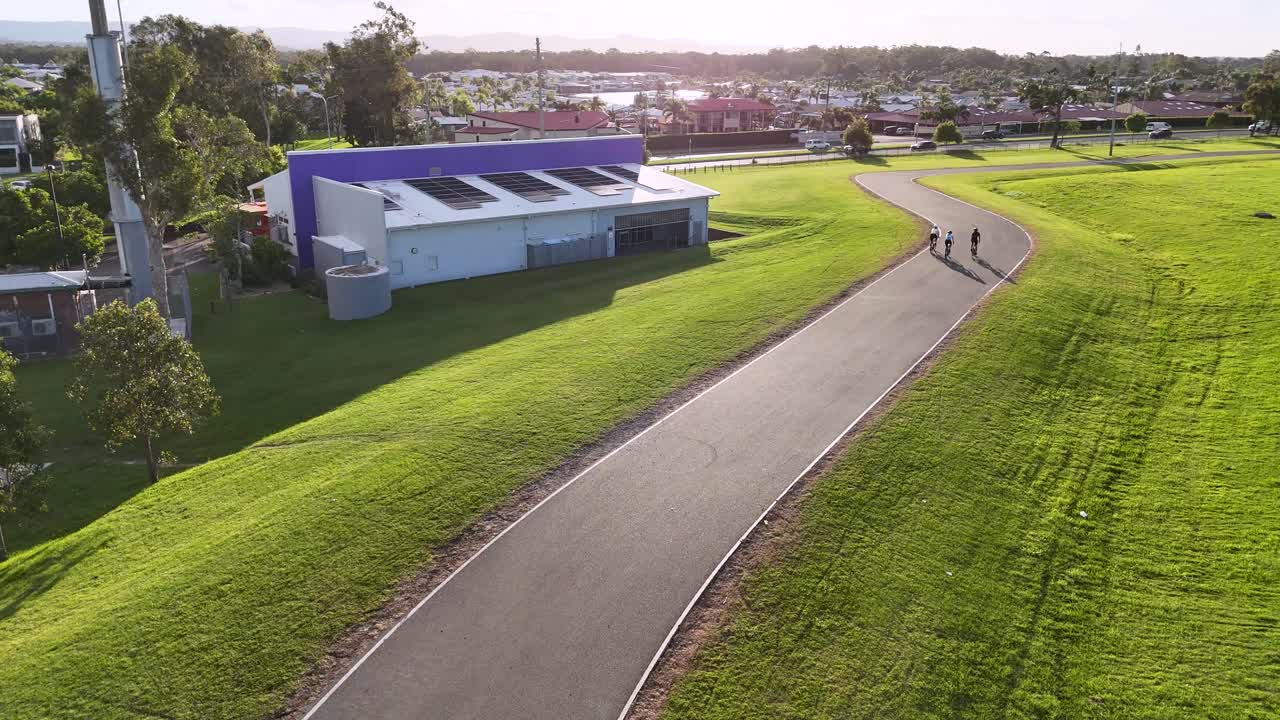 Aerial view of cyclists training on a winding track at sunset, showcasing vibrant green landscapes and dynamic movement