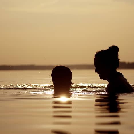 silhouette of a woman and two boys in river at dusk. children having great time with their mother inside the water at summer time in the evening.