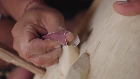 las manos de los talladores con papel de lija lustrando la máscara de barong bangkal
