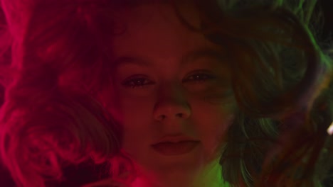 artistic portrait of girl behind colored glass with dramatic lighting close up portrait of a girl viewed through tinted or reflective glass illuminated by red green and golden light for a cinematic surreal effect