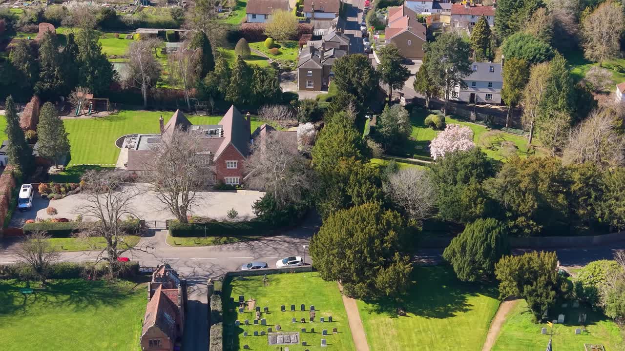 Ponny och kärra korsar Hertingfordburyvägen medan drönare flyger framåt ovanför Hertingfordbury by, kyrka och kyrkogård, Hertfordshire, England en klar dag.