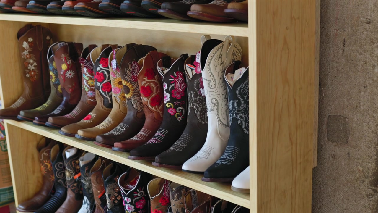 Handgefertigte Cowboystiefel, ausgestellt auf einem Kunsthandwerkermarkt in Tapalpa Pueblo Mágico, mit farbenfroher Blumenstickerei und traditionellem Westernschuhwerk, Jalisco, Mexiko. Statische Aufnahme