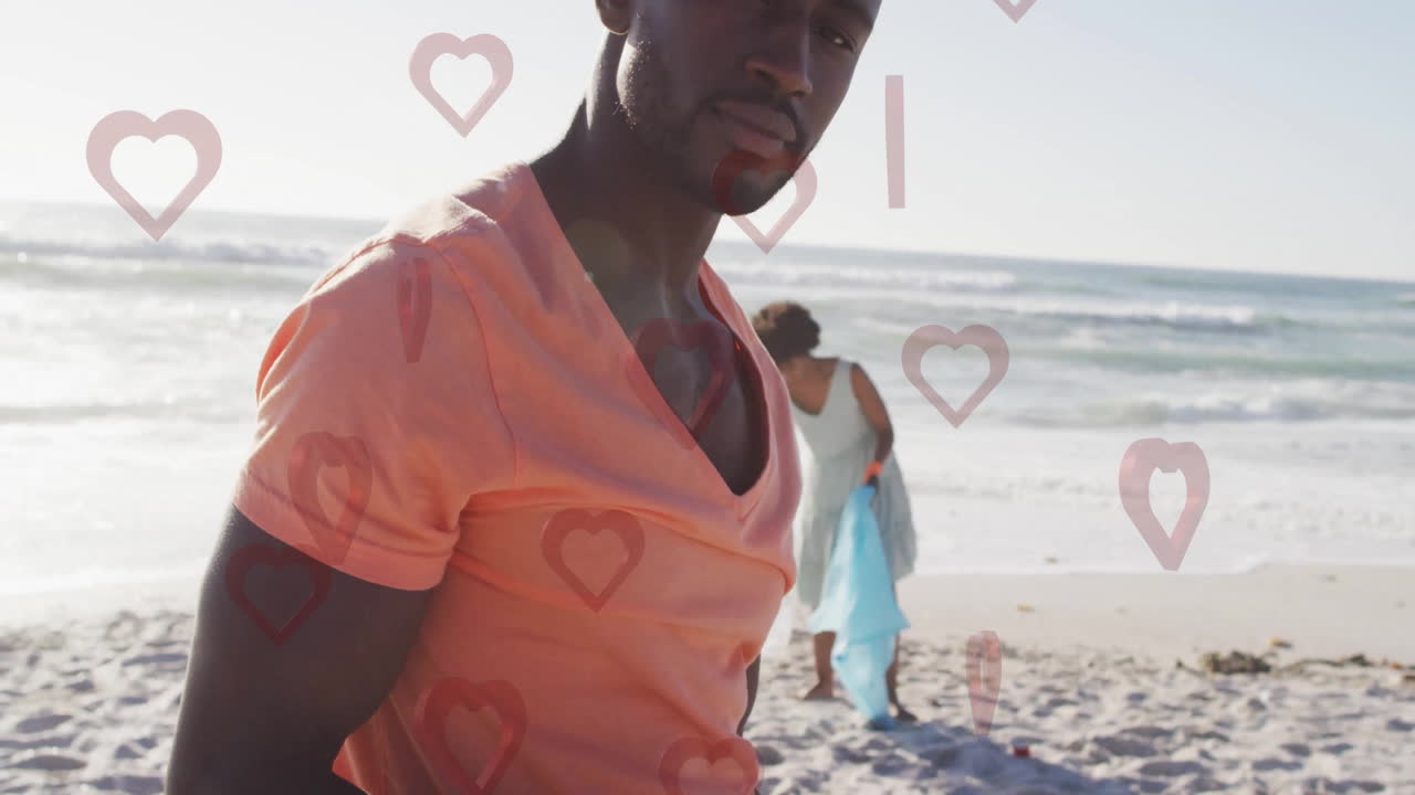 On beach, man in orange shirt with heart animation overlaying scene