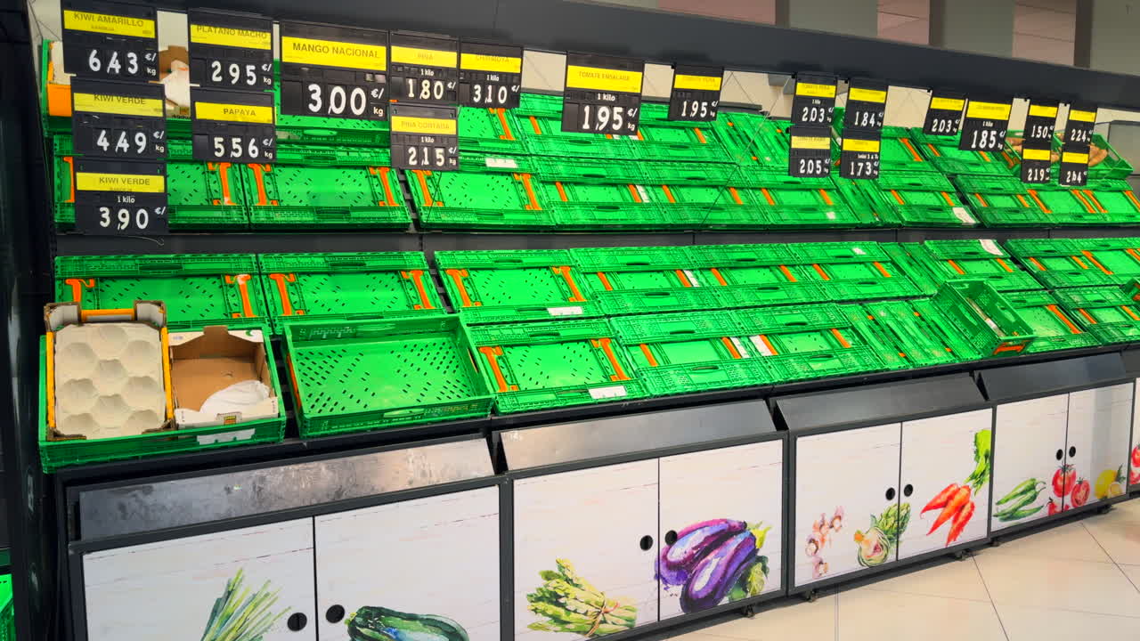 Empty green plastic crates in a supermarket with price tags, suggesting food shortages and supply chain problems.