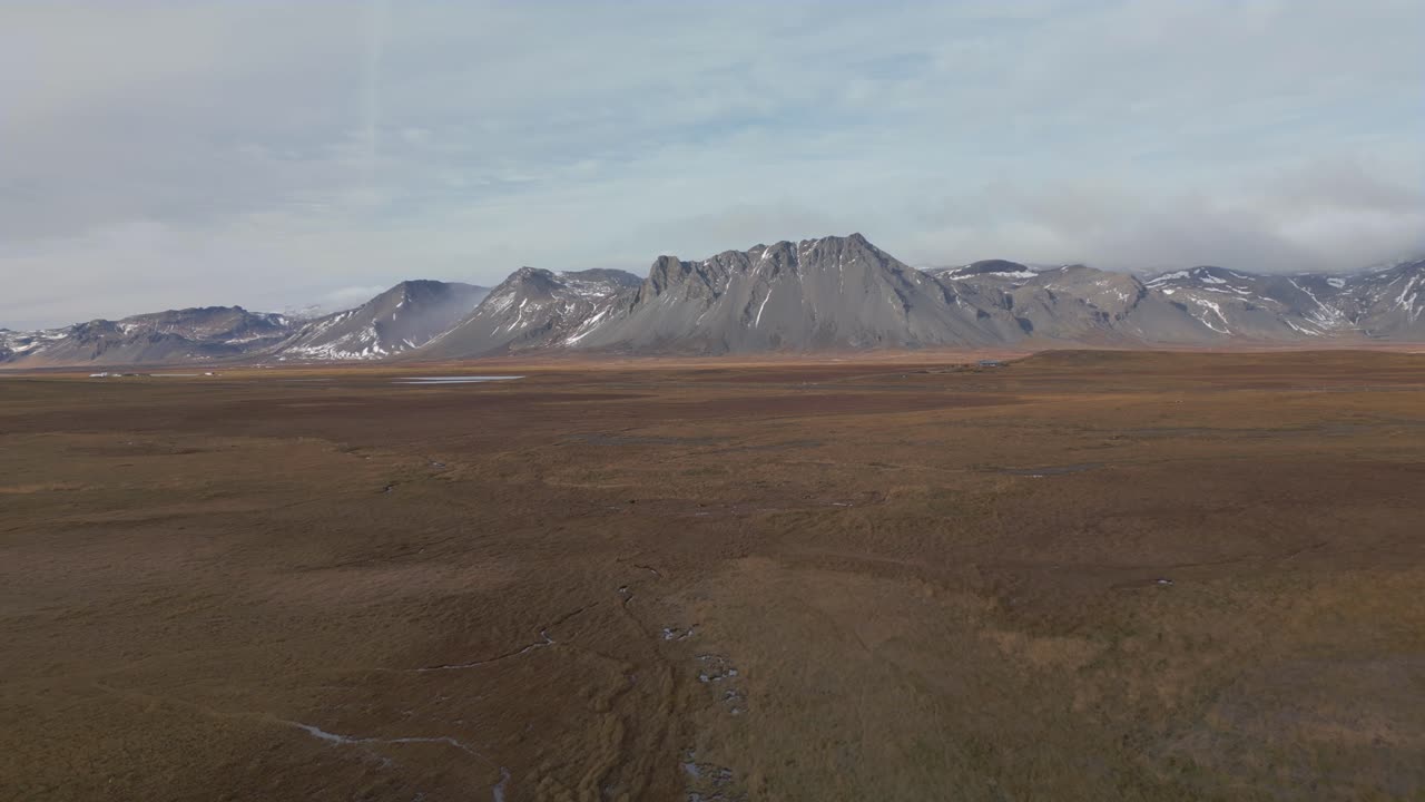 Flyr mot dramatisk fjellkjede som ruver i øde, islandsk landskap