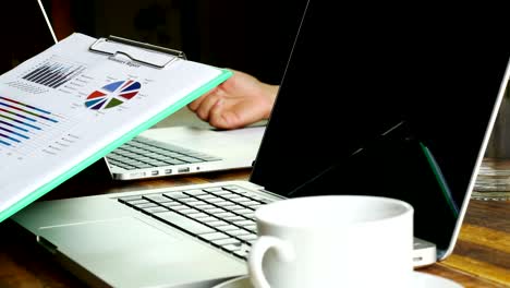 trabajador buscando informe de verano y escribiendo portátil con café de bebida.