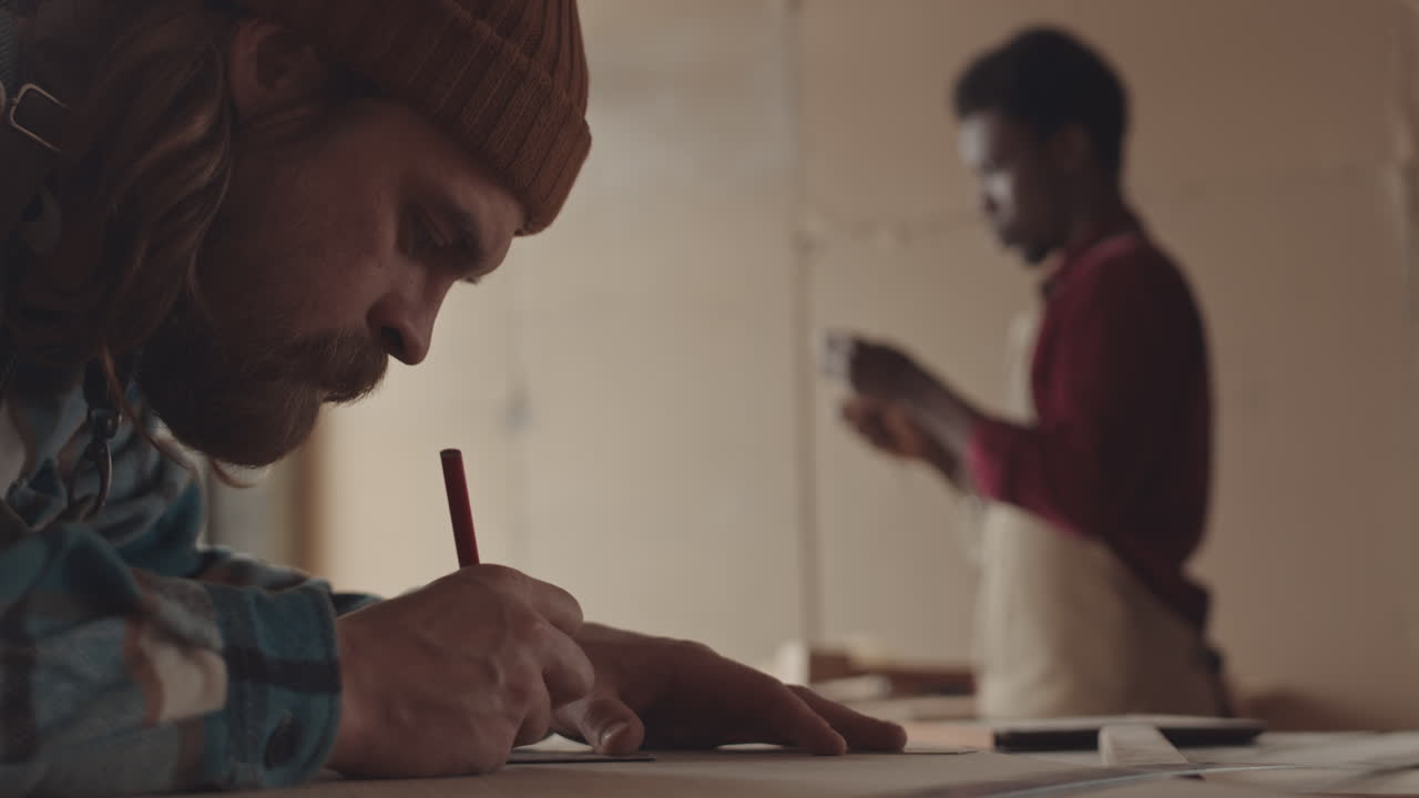 Caucasian Craftsman Drawing on Piece of Wood in Workshop