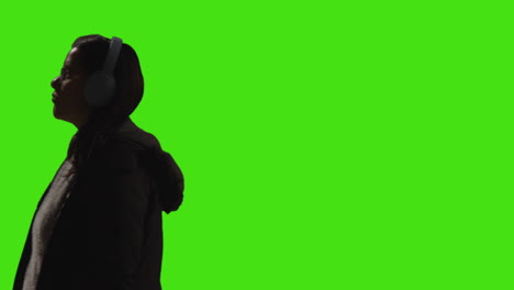 woman wearing wireless headphones streaming music from mobile phone walking across frame against green screen