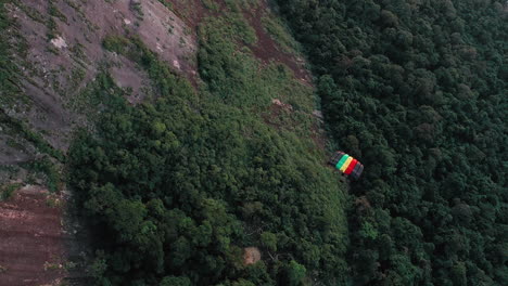 aerial view of parachuter gliding down over large rock face and lush green forest