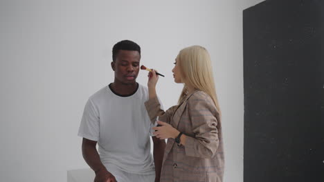 Una-Maquilladora-Hace-Maquillaje-En-Una-Sesión-Fotográfica-Profesional-De-Un-Jugador-De-Fútbol.-Estudio-Fotográfico-Con-Equipo-Profesional-Y-Equipo-De-Trabajadores.-Equipo-Discutiendo-La-Dirección-De-Producción