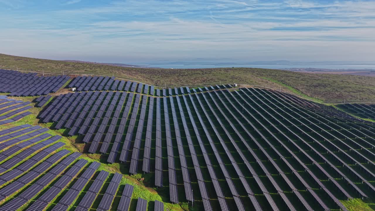 Stort solcellepanelanlæg på en bakketop under en blå himmel med skyer