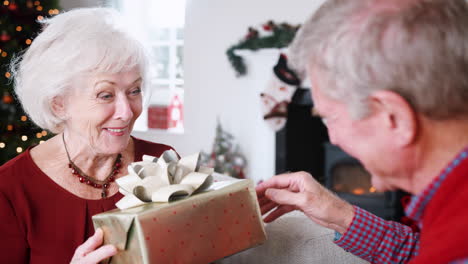 senior couple exchanging gifts as they celebrate christmas at home together