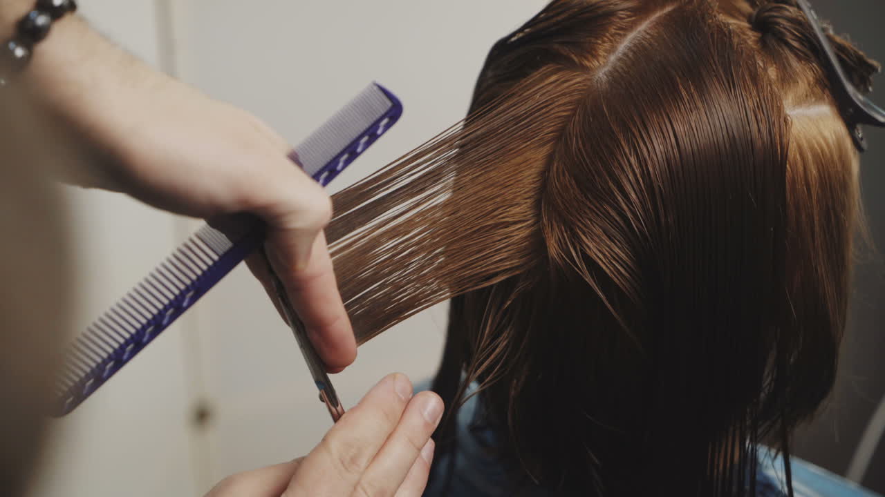 Young male hairdresser working. Trimming brown hair with scissors. Close-up