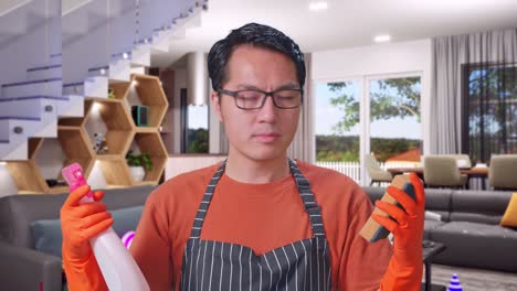 close up de ama de casa masculina asiática con un delantal mirando el spray y la esponja de cocina en las manos y luego sacudiendo la cabeza en la casa